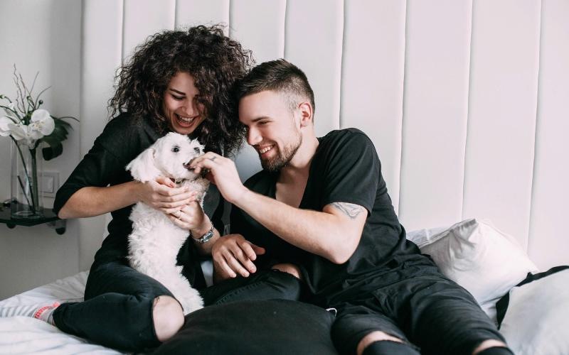 a man and woman sitting on a bed playing with a dog